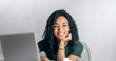 Frau mit Brille und Laptop lächelt am Schreibtisch