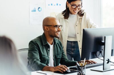 Zwei Personen im Büro arbeiten lächelnd am Computer zusammen