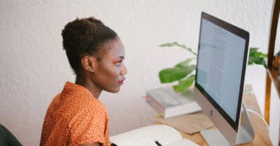 Frau mit lockigem Haar lernt mit Microlearning am Schreibtisch mit iMac